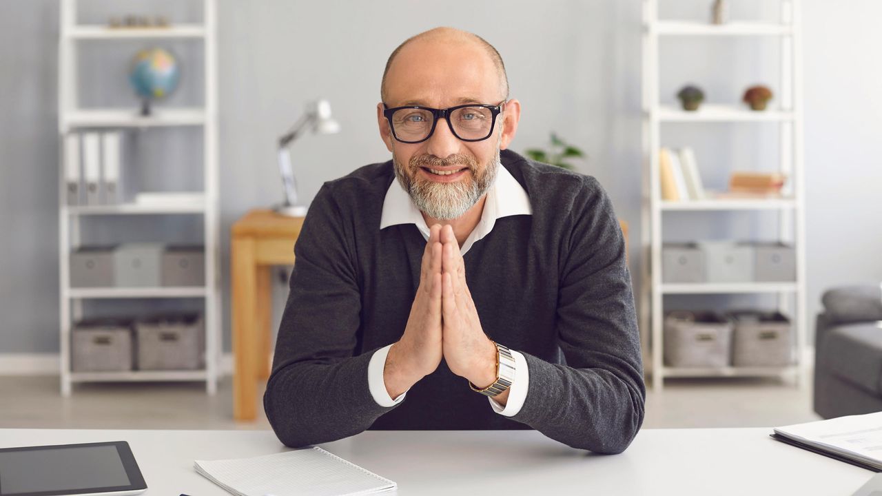 A friendly looking financial adviser sits at a desk.