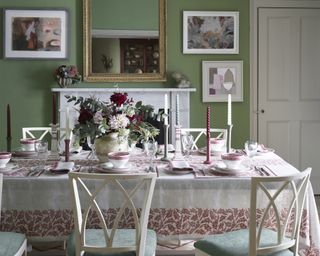 A dining table decor idea with red and white tablecloth and flowers, with green walls and white furniture