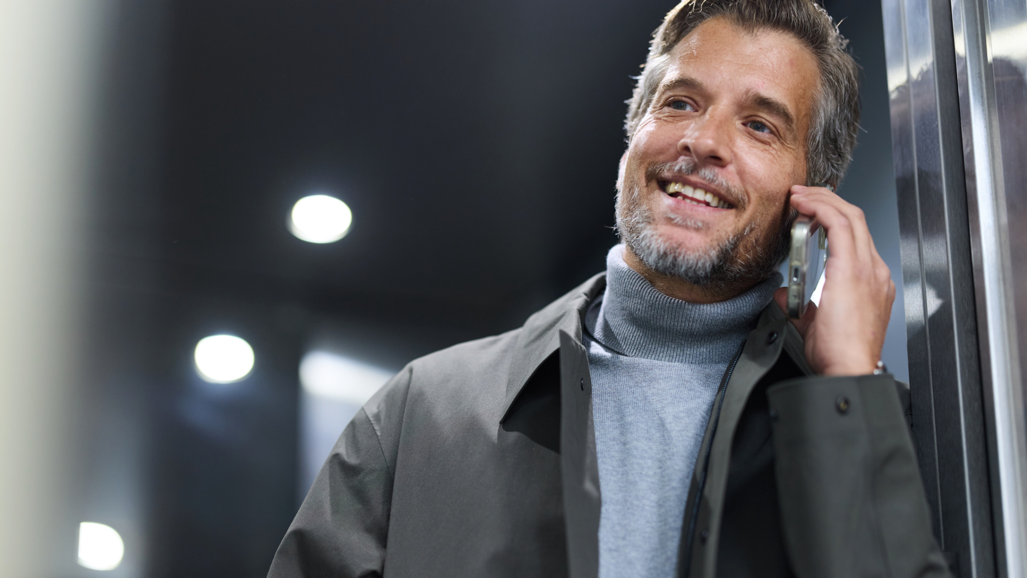 A man, smiling, while taking a call on their smartphone.