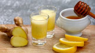two cups of ginger shots, a pot of honey, lemon slices and root ginger