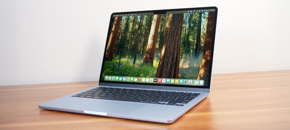 Apple MacBook Air 13-inch M4 on a wooden table with the display showing the macOS Sequoia desktop.