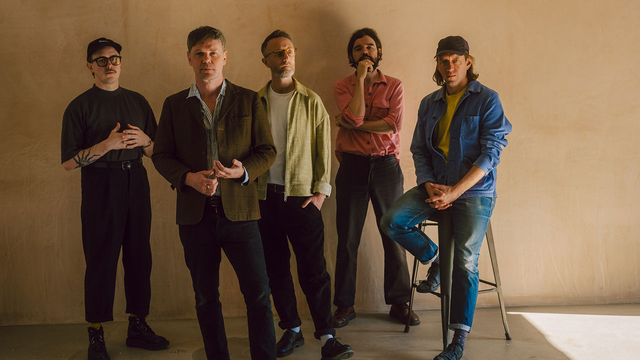 A portrait of the band Idlewild stood in front of a light brown wall