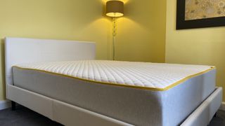Image shows the Eve Premium Hybrid mattress placed on a white faux leather bed frame in a yellow bedroom