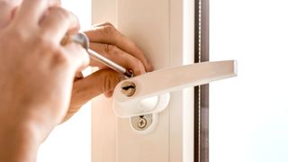 Hand with screwdriver removing screw from window handle on a white UPVC window