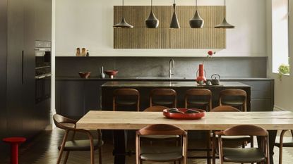 black kitchen with white walls, light wood kitchen table and matching dark wood bar stall and dining chairs with dark green seat cushion