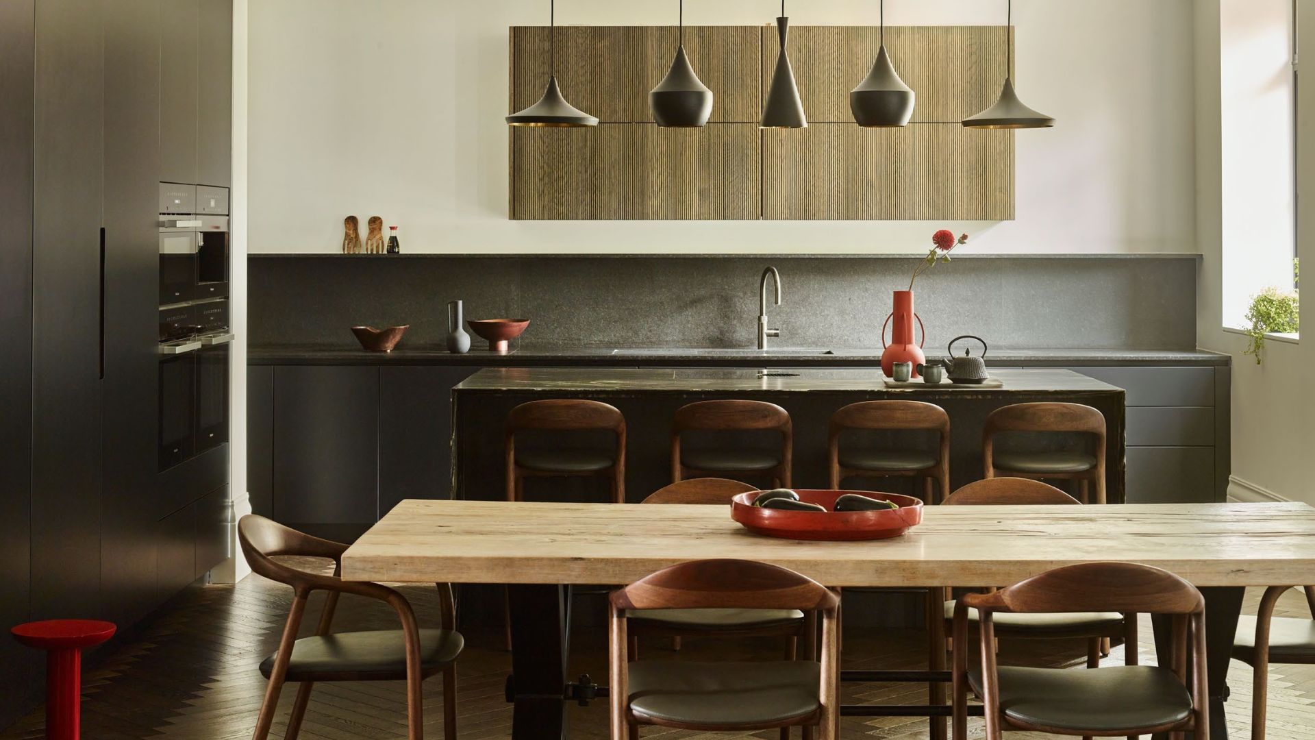 black kitchen with white walls, light wood kitchen table and matching dark wood bar stall and dining chairs with dark green seat cushion