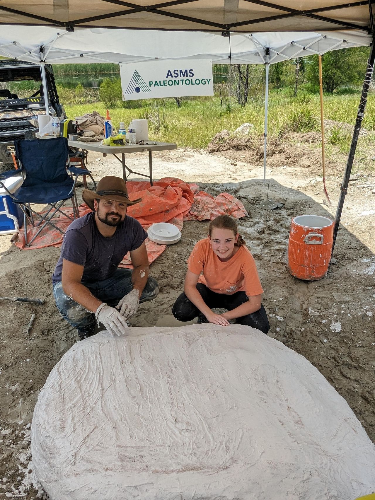 man and woman crouching behind a large whale skull beneath a tent