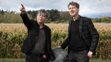 Two people stand in front of a corn field holding a meteorite 