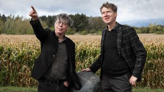 Two people stand in front of a corn field holding a meteorite 