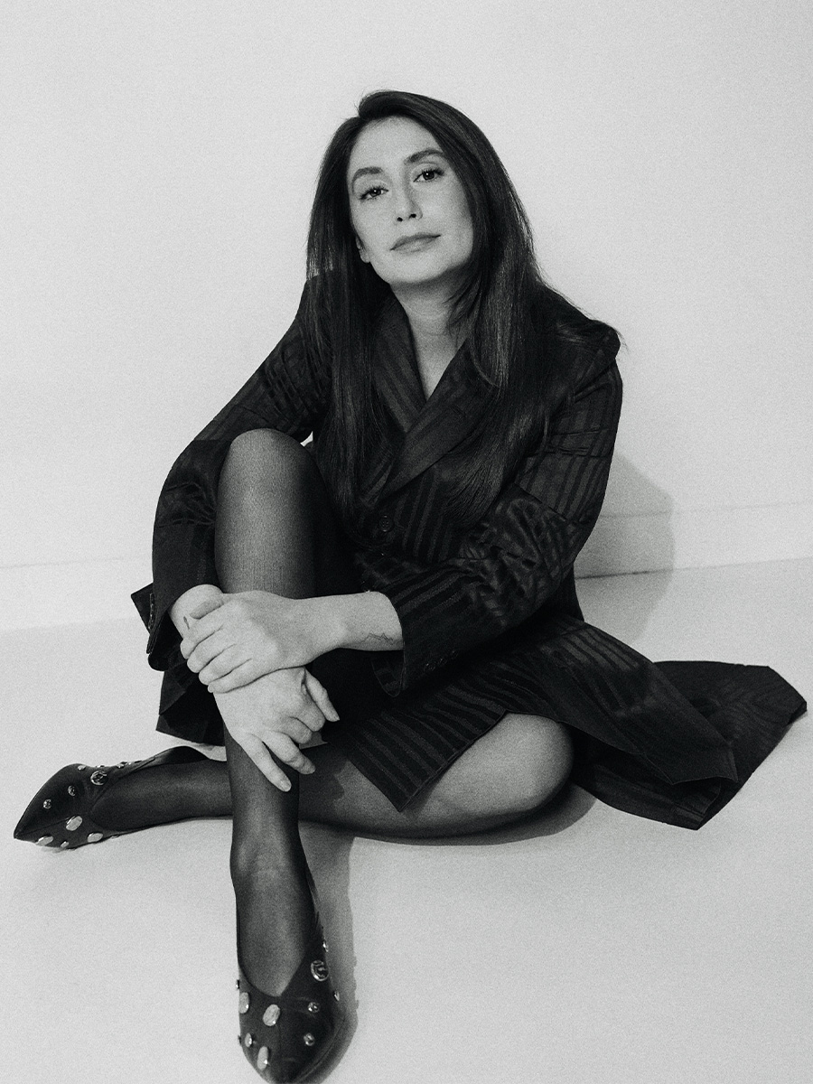 Images of Rooster actress Charly Clive shot by Emily Soto. The black and white photos show Charly sitting on the ground wearing a black pinstripe blazer dress with black heels with metal detailing.