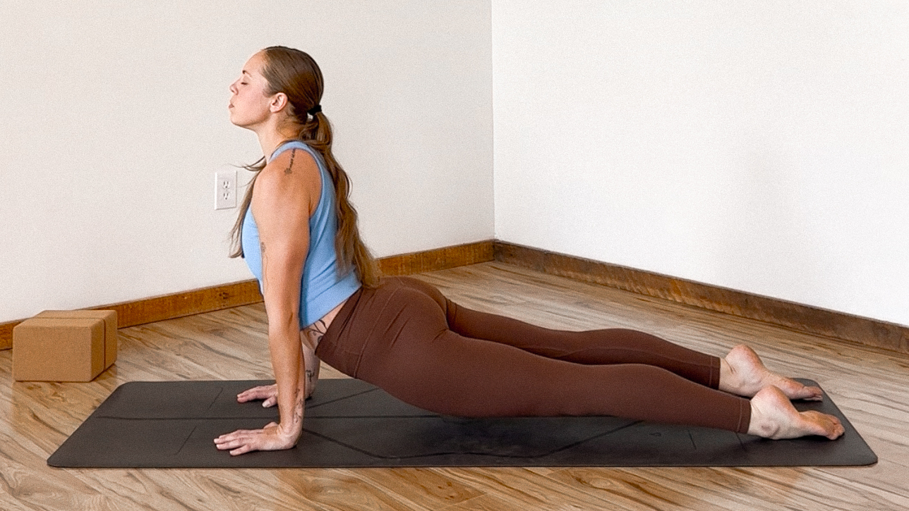 Woman in brown leggings and blue tank top demonstrates yoga pose