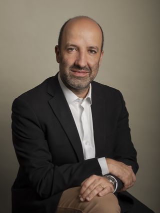 photo of a smiling man with a short beard wearing a suit jacket and button down shirt