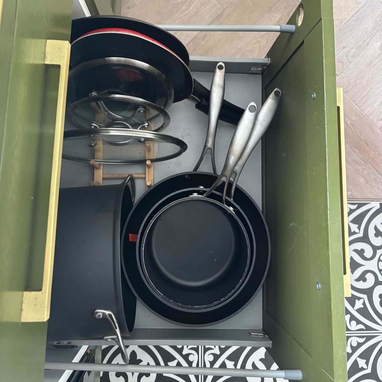 Pots and pans organised in a dish rack in a green kitchen cupboard