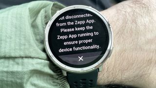 Close-up of the Amazfit Active 2 in a user's hand with a warning screen that says that the Zepp companion smartphone app must remain open to use the watch's AI voice assistant