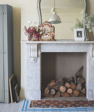 Cozy fireplace with marble, wooden logs, big mirror and floral arrangements