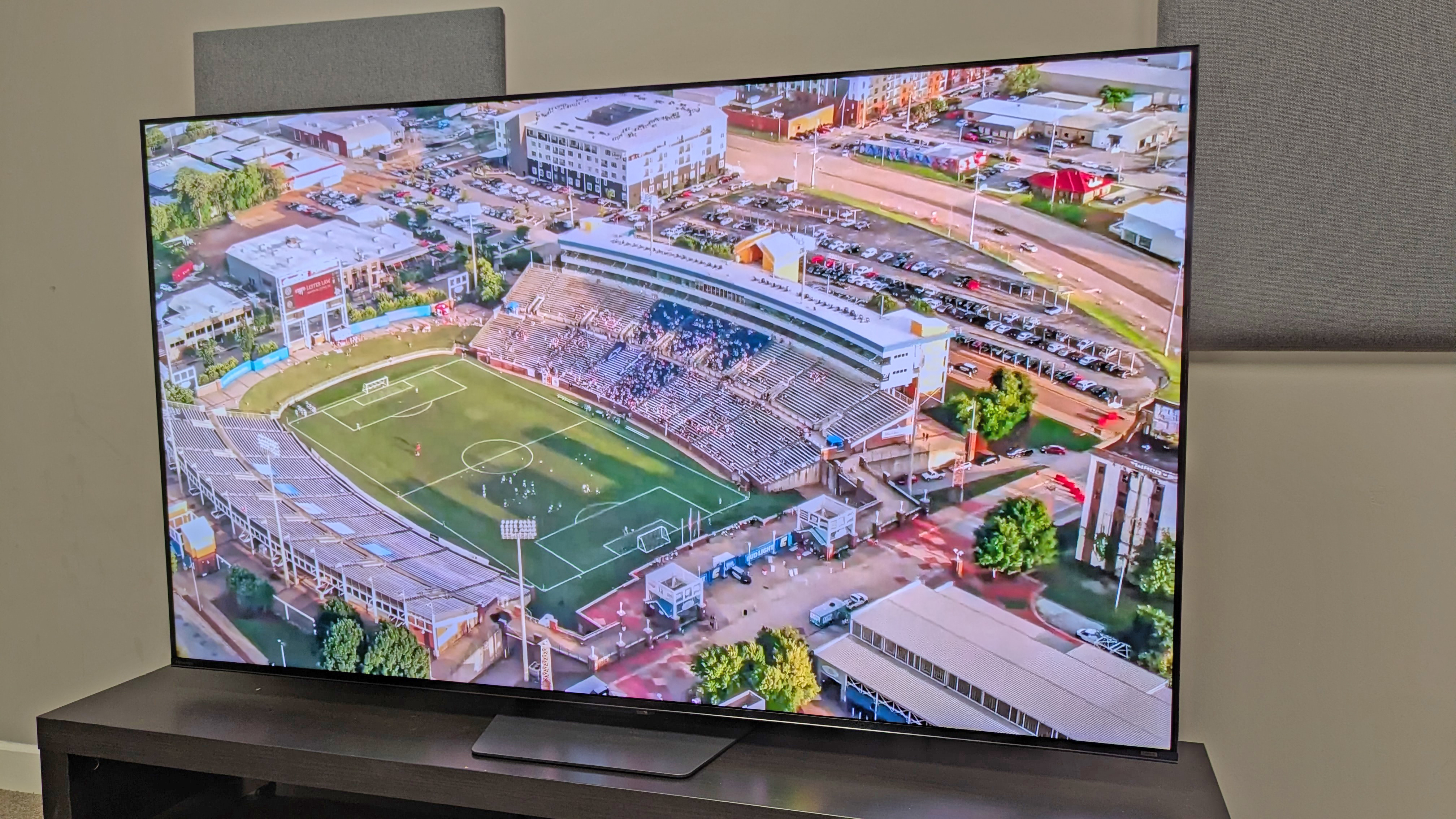 Hisense U7S Pro TV with an aerial shot of an outdoor football stadium in the day on screen, with photo taken from right angle
