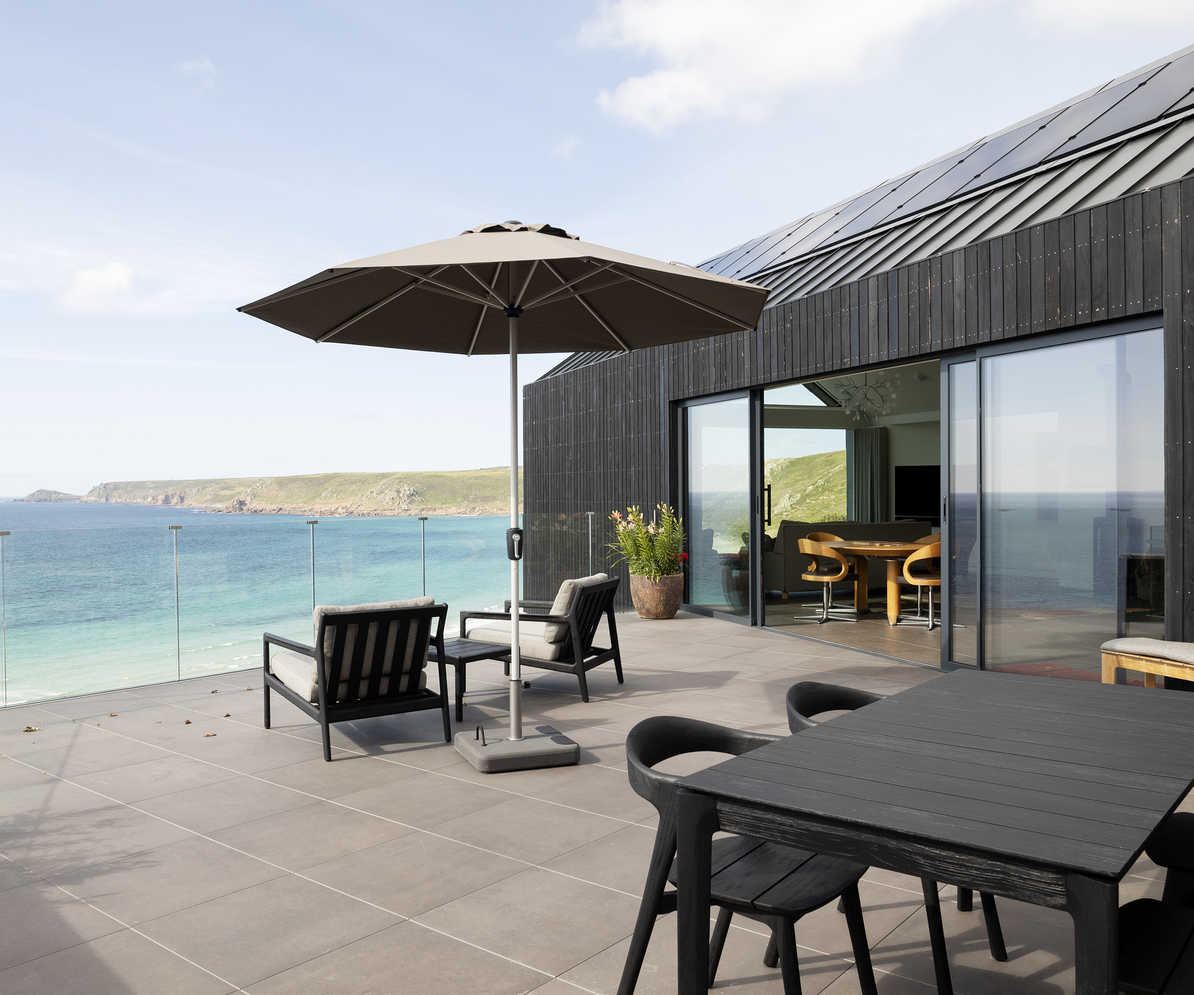 A sunny terrace with parasol and lounge chairs and outdoor dining table with sea views in the background