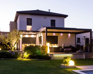 Exterior shot of a garden with modern property showing lights on inside and security lights