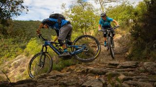 Two eMTBers negotiate a technical turn on a rooty trail