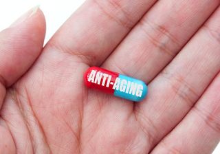 A person holds a pill marked "anti-aging" in their hand.