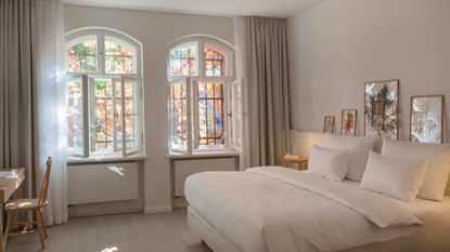 white bedroom with white bed and trees outside windows