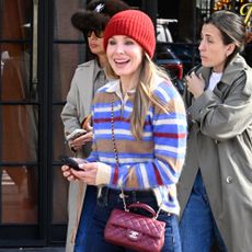 Kristen Bell walks outside wearing a striped polo jumper with indigo jeans, a burgundy Chanel bag and black slim-line leather trainers.