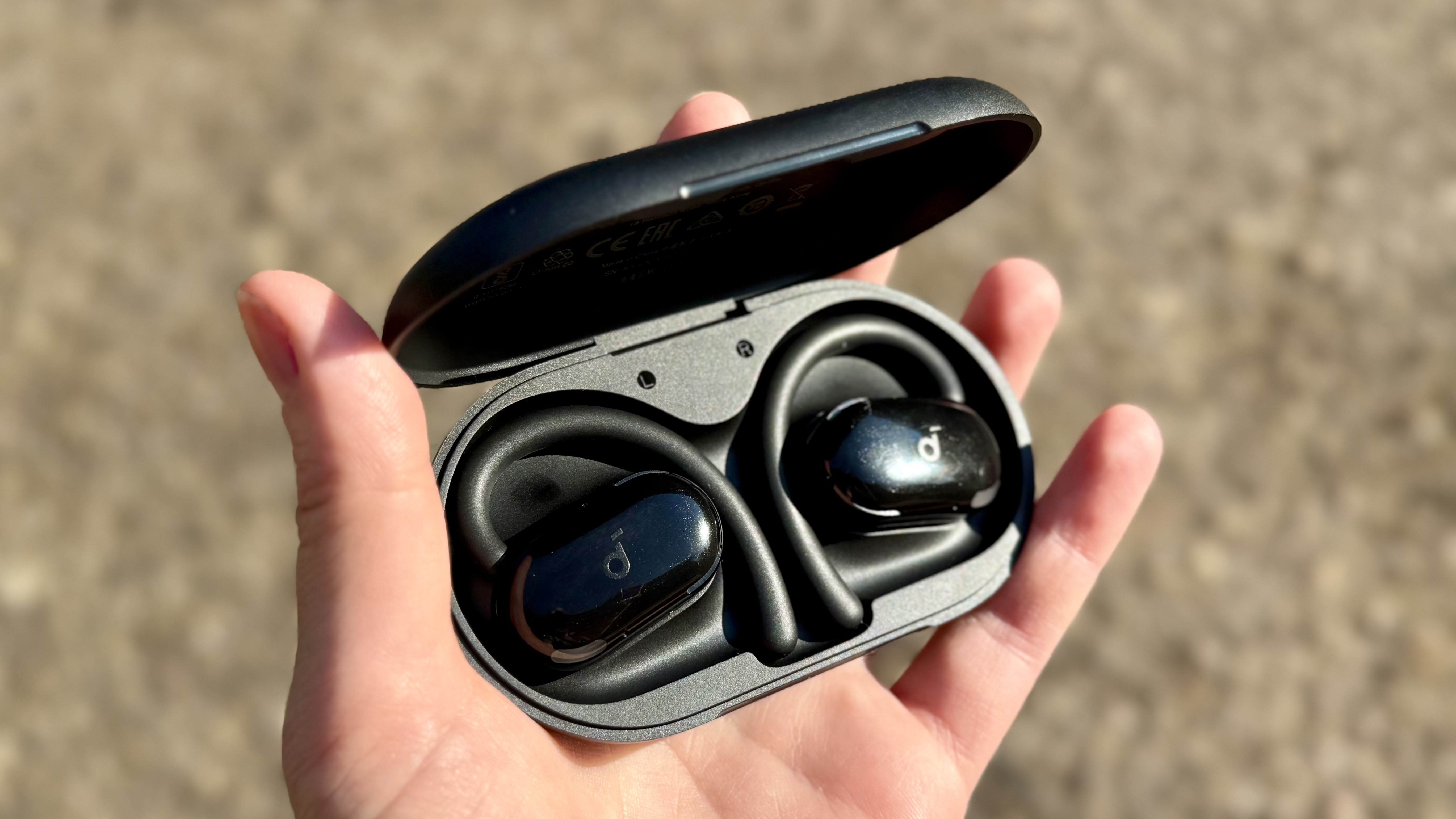 A hand holding the Soundcore Anker V20i earbuds in their charging case