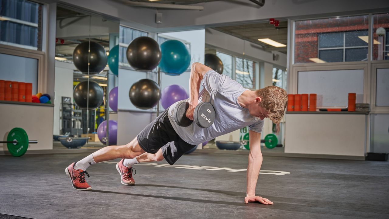  Male cyclist in a plank position pulling a dumbbell up to the right side of his ribcage