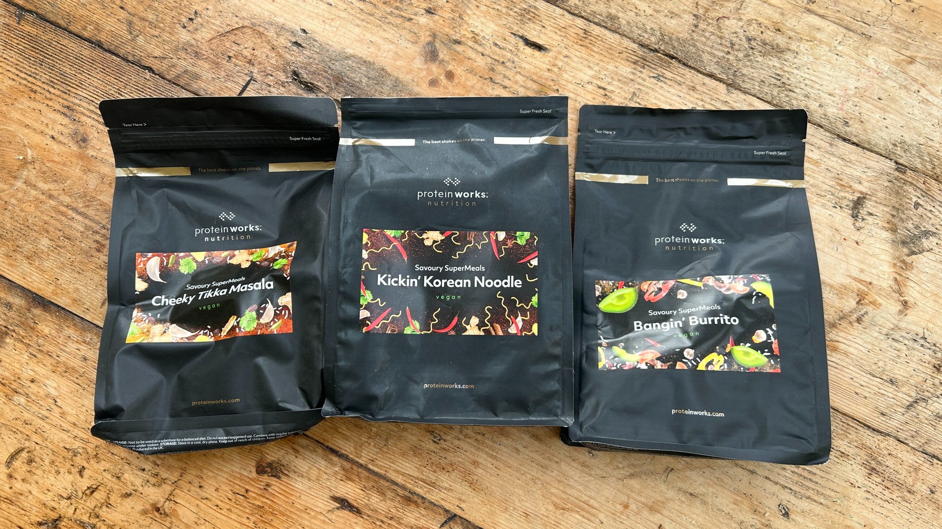 Three ready meal packets from the Protein Works arranged in a line on a table