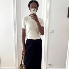 influencer Sylvie Mus poses for a mirror selfie wearing a cream short sleeve sweater top and black skirt