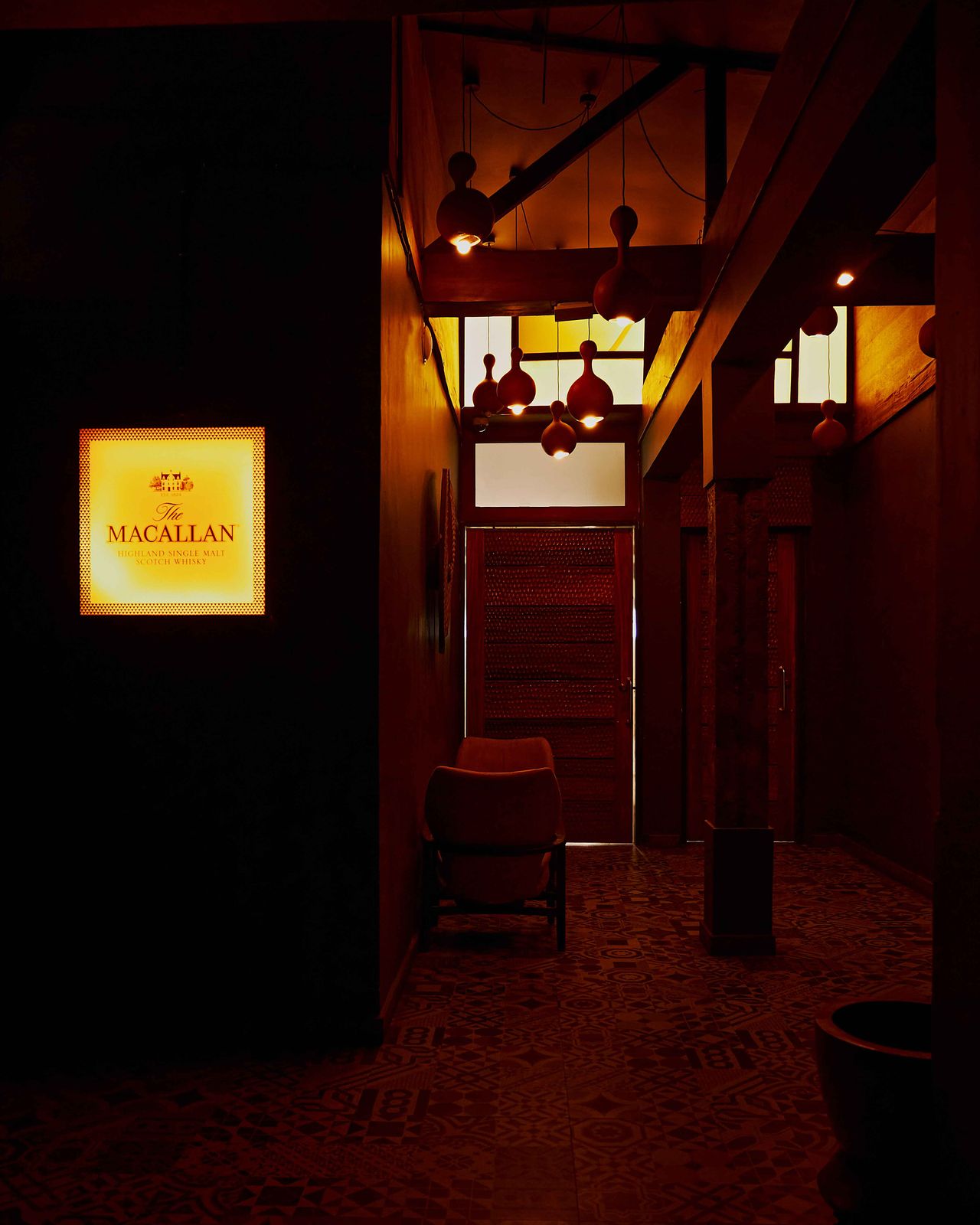 The warm interiors of a private members' club boast textured flooring covered in different tiles, pending lanterns, and a back-lit sign.