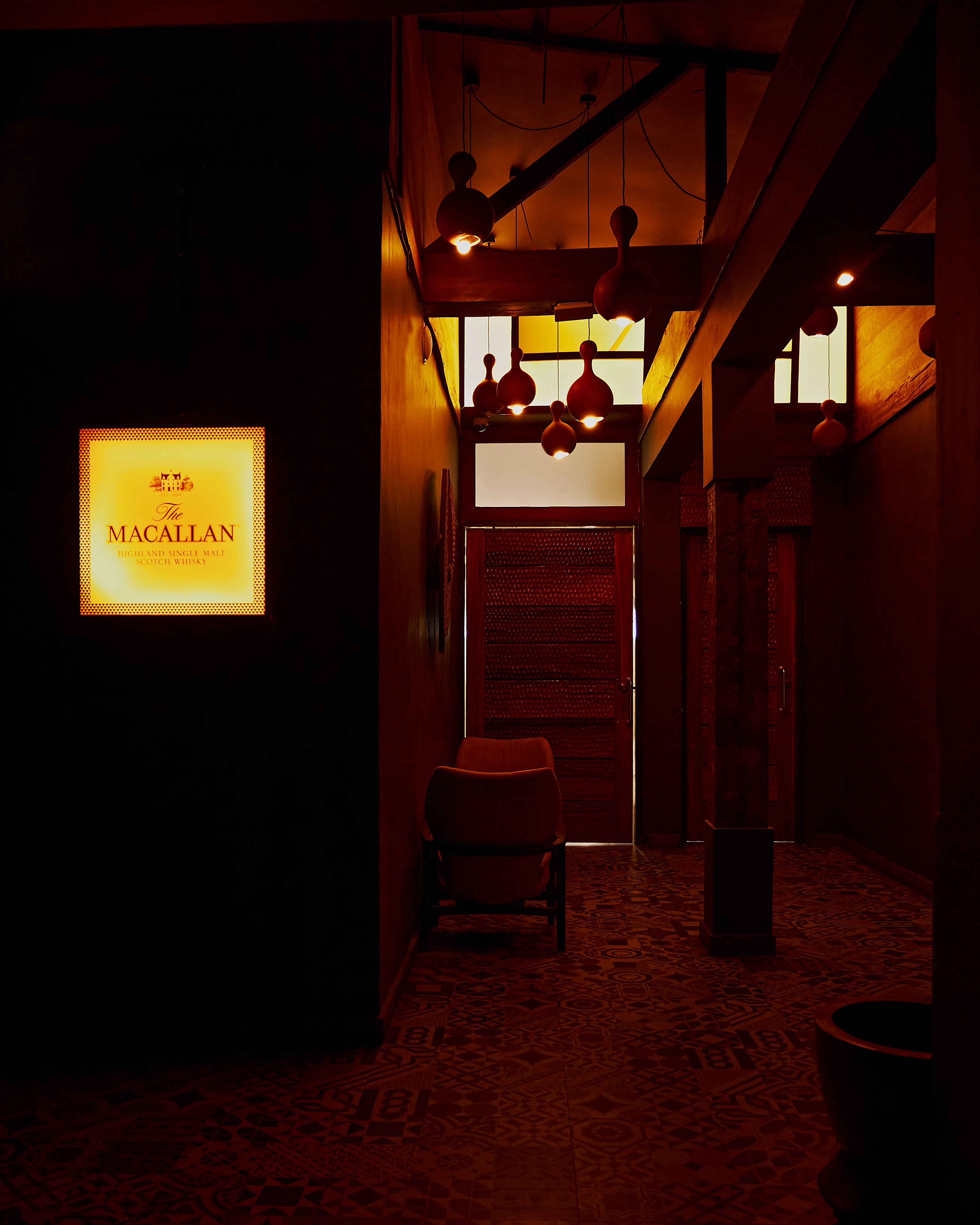 The warm interiors of a private members' club boast textured flooring covered in different tiles, pending lanterns, and a back-lit sign.