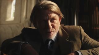 Daniel Craig leans over smiling half obscured in shadow in Wake Up Dead Man: a Knives Out mystery.