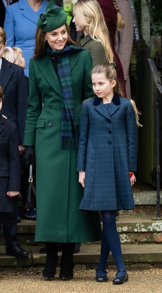 Princess Kate wearing a long green coat and blue and green scarf standing next to Princess Charlotte in a plaid coat and blue tights outside church