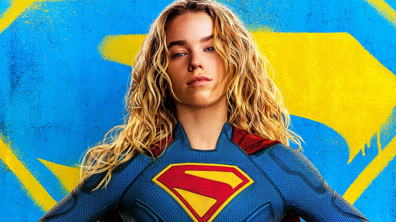 Supergirl in costume in front of blue and yellow symbol in Supergirl poster