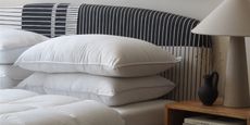 a striped bed head with undressed pillows, and a lamp on a side table