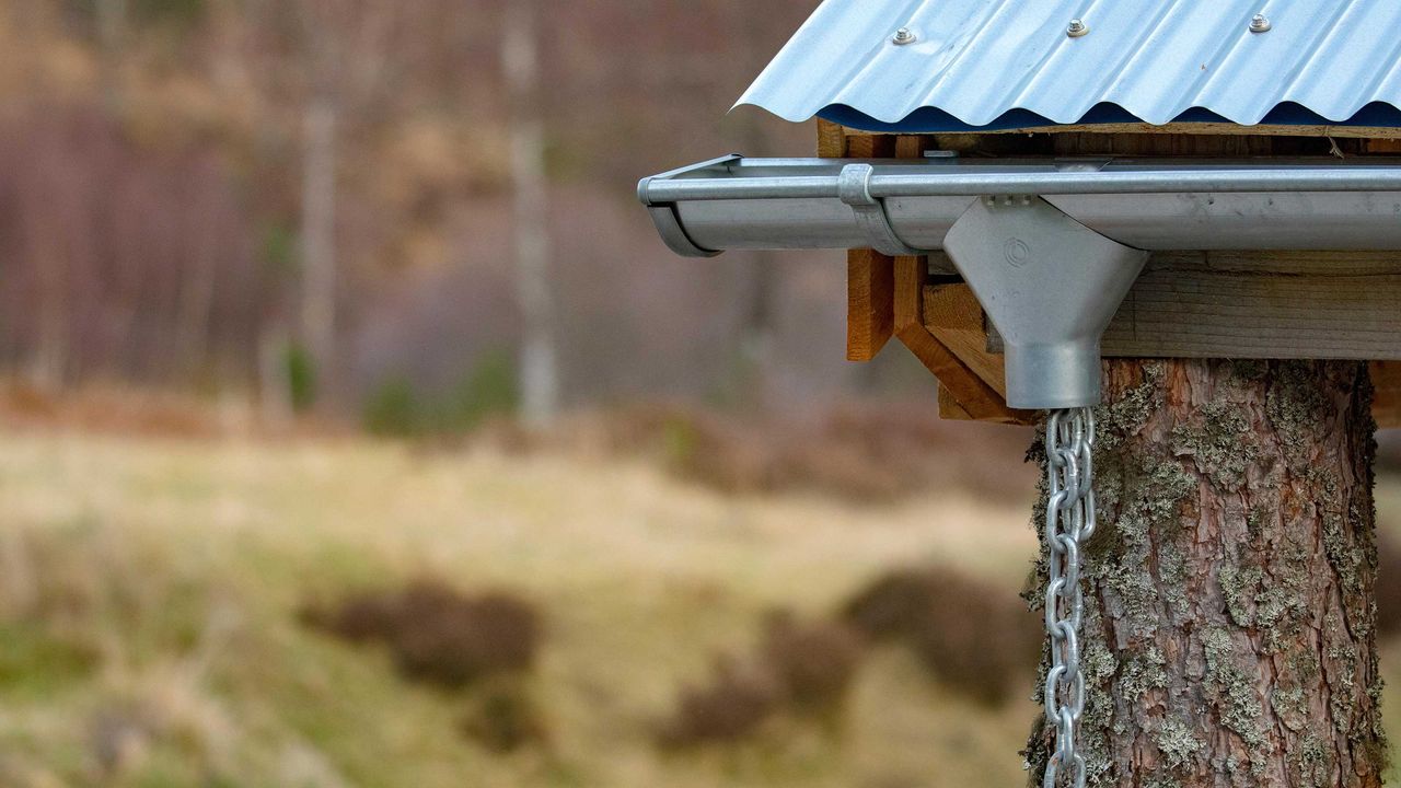 A rain chain downspout or down pipe used to harvest or move water away without drainage on a tin roof building