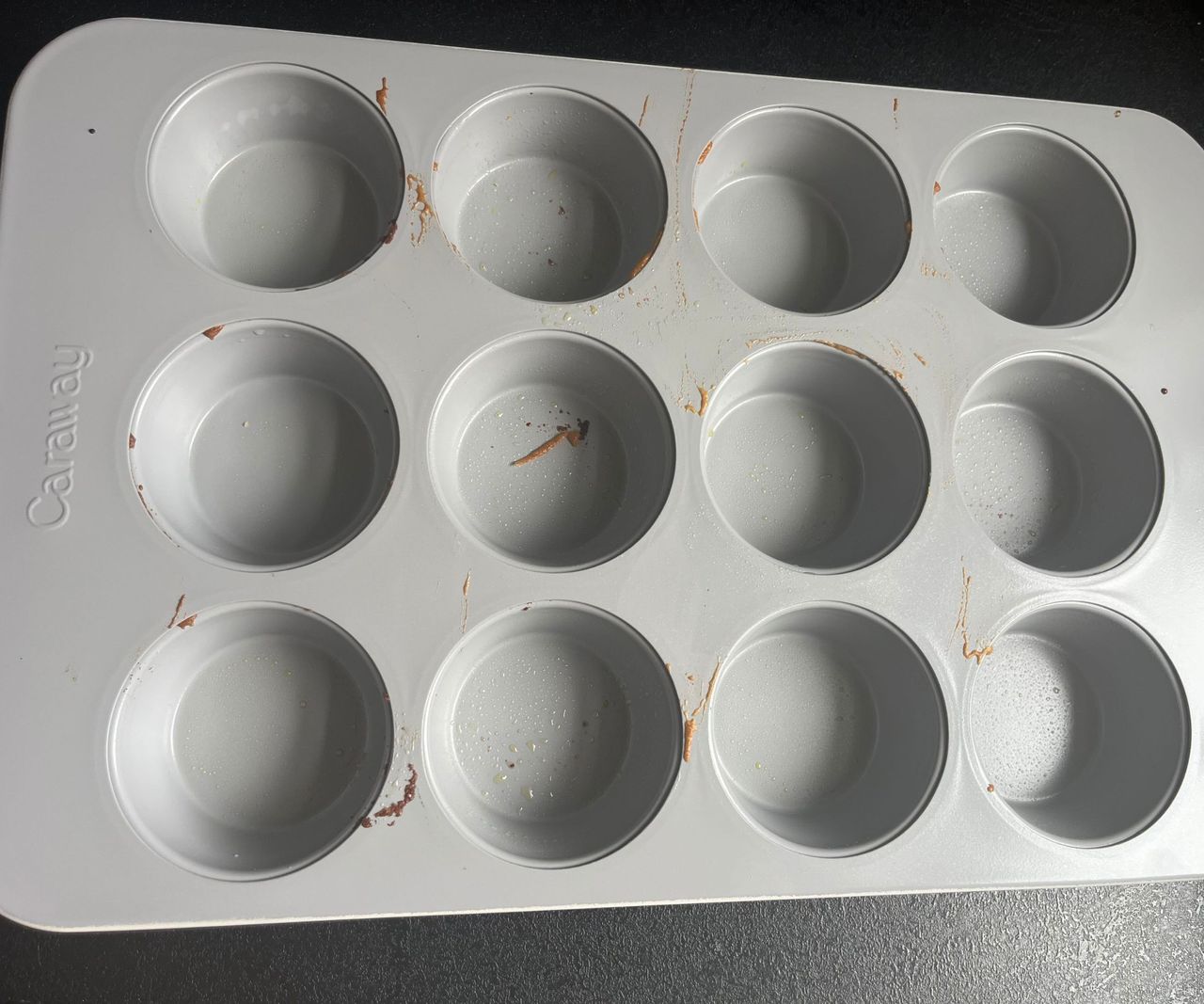 A grey 12-hole muffin tin with cake batter splatters on it