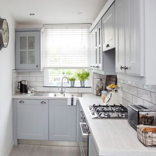 A small L-shaped kitchen with light grey cupboards and white brick wall tiles