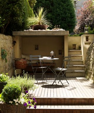 An example of small garden ideas with a deck leading to stone steps and featuring a small garden dining area and shaded nook seat.