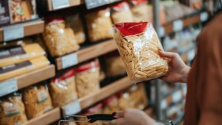 woman picking up a packet of gluten-free pasta at the grocery store