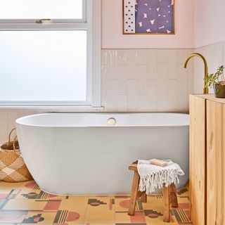 bathroom with a modern white bath tub, blush pink walls and graphic patterned floor tiles