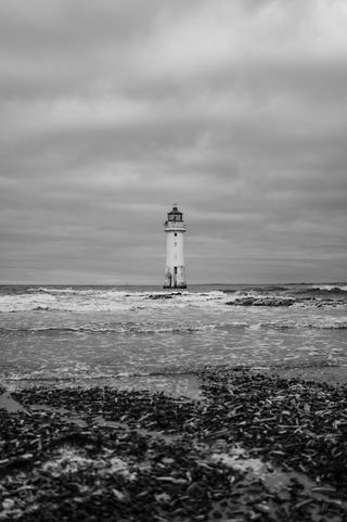 A lighthouse out at sea seen from the beach with stormy waves breaking all around it