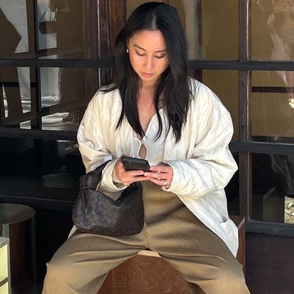 style influencer Jordan Risa wearing a white keyhole tie-front top, a woven brown bag, and pliss&eacute; tan pants