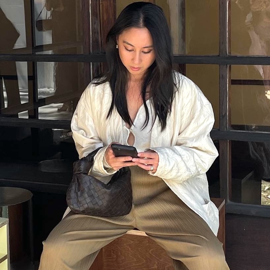 style influencer Jordan Risa wearing a white keyhole tie-front top, a woven brown bag, and pliss&eacute; tan pants