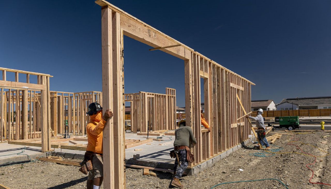 Contractors raise a framed wall on a house under construction.