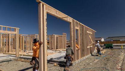 Contractors raise a framed wall on a house under construction.