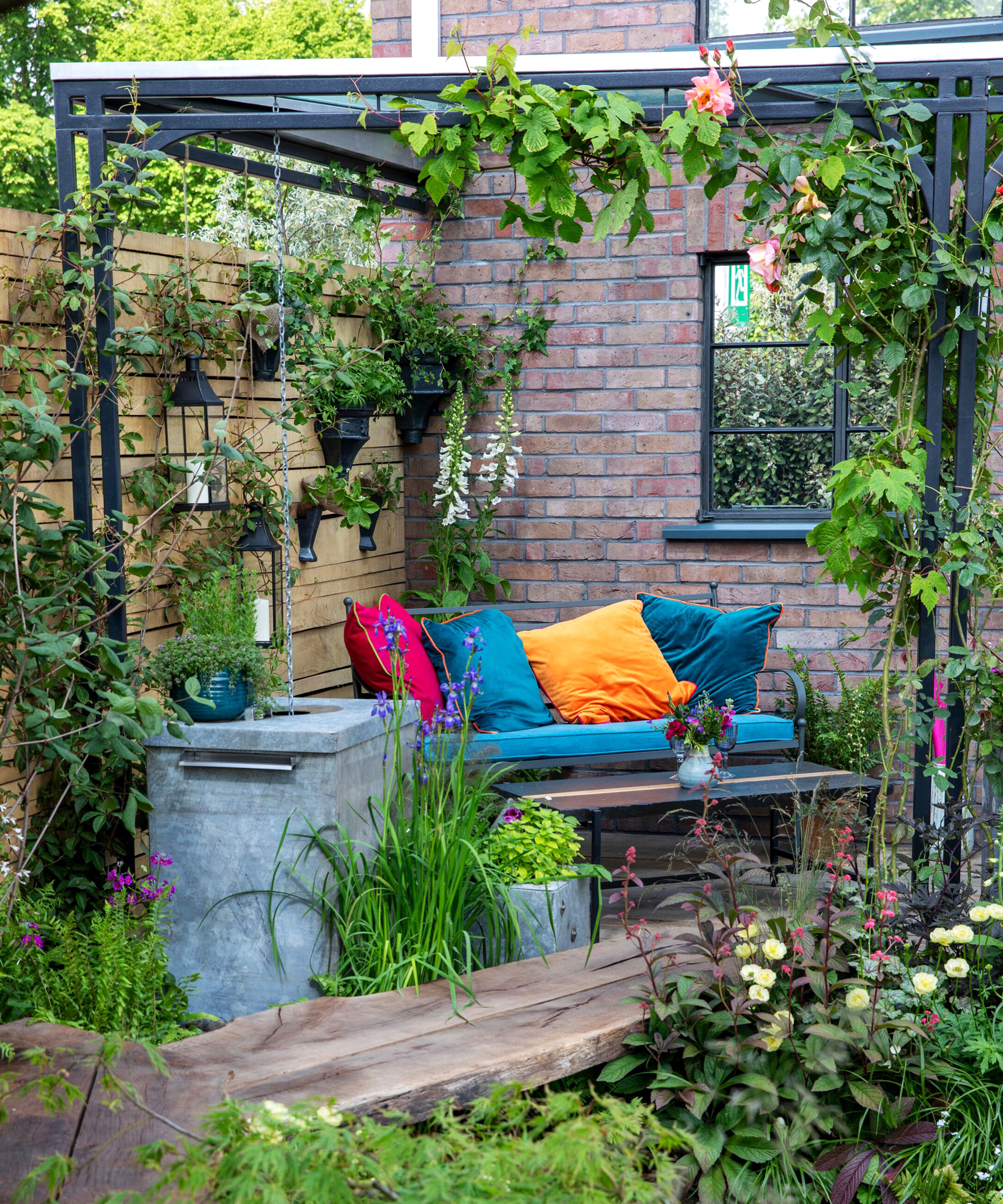Corner of small garden with pergola and garden furniture, and lots of plants