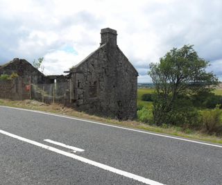 An old stone cottage with crumbling walls next to a road