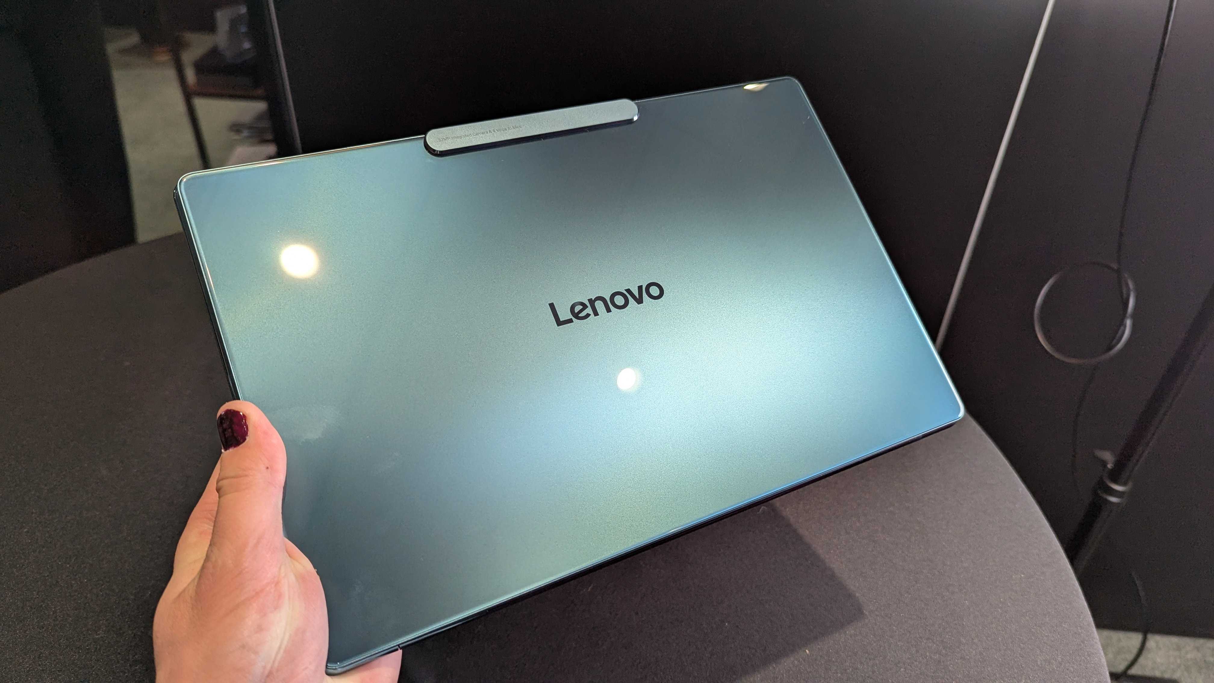 The Lenovo Yoga Slim 9i 14 (Gen 10) held in the hand, showing its glossy glass lid.